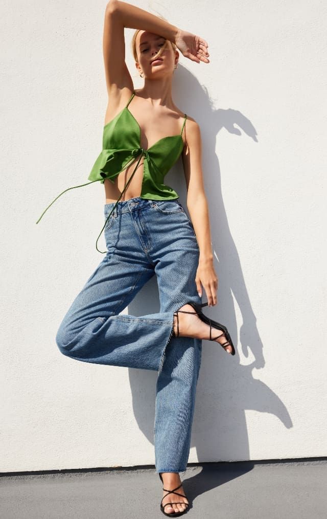 A model wears a green satin fly-away cami with blue jeans.