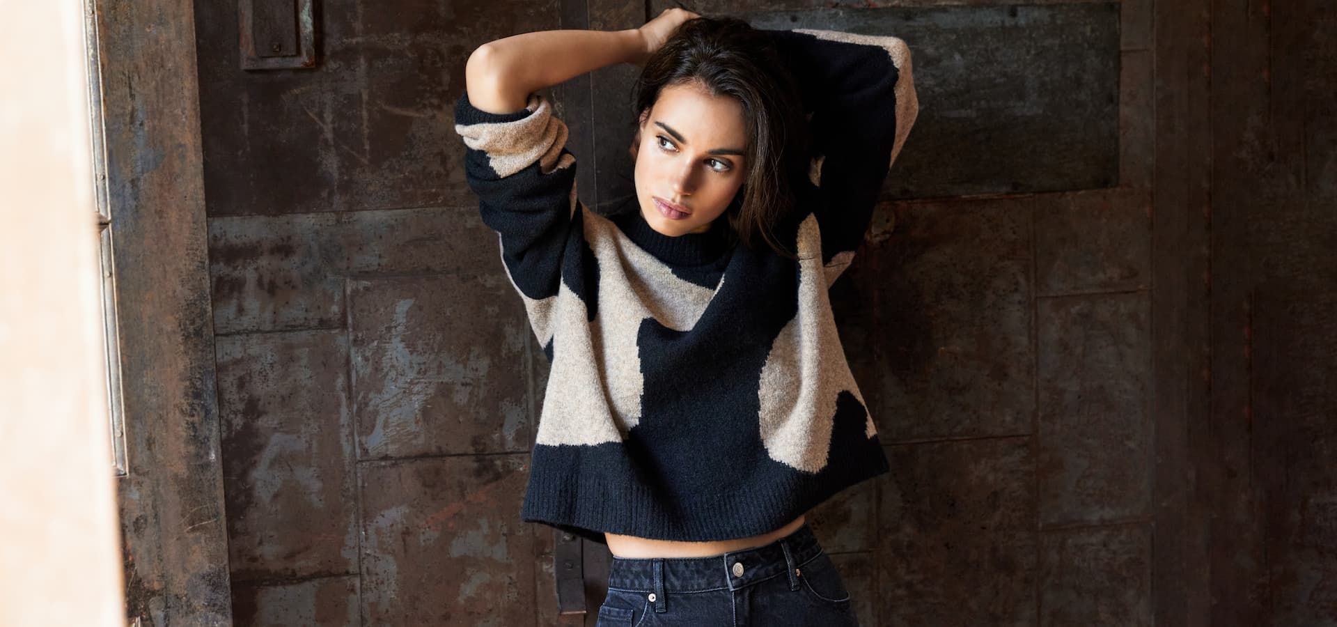 A model wears a black and beige printed sweater with black jeans.