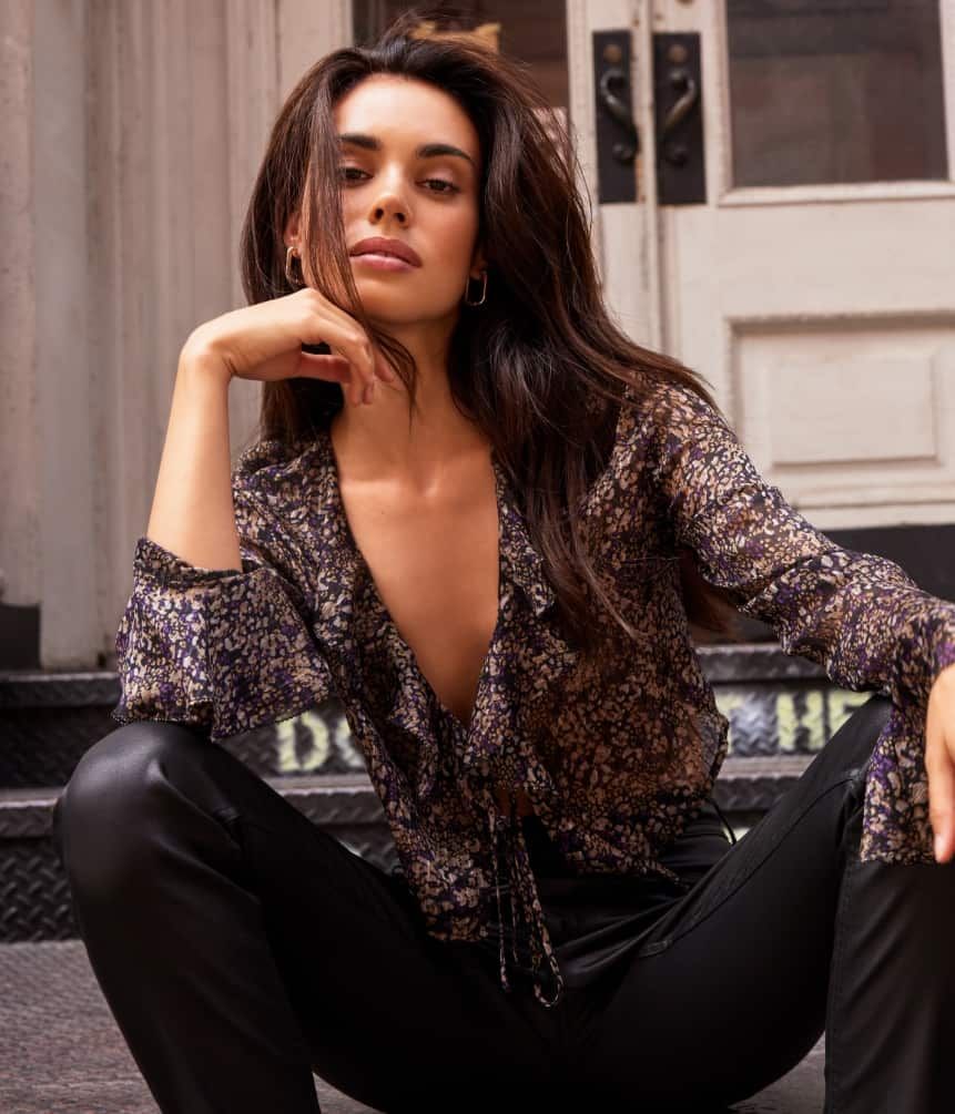 A model wears a frilled floral blouse with black faux leather pants.