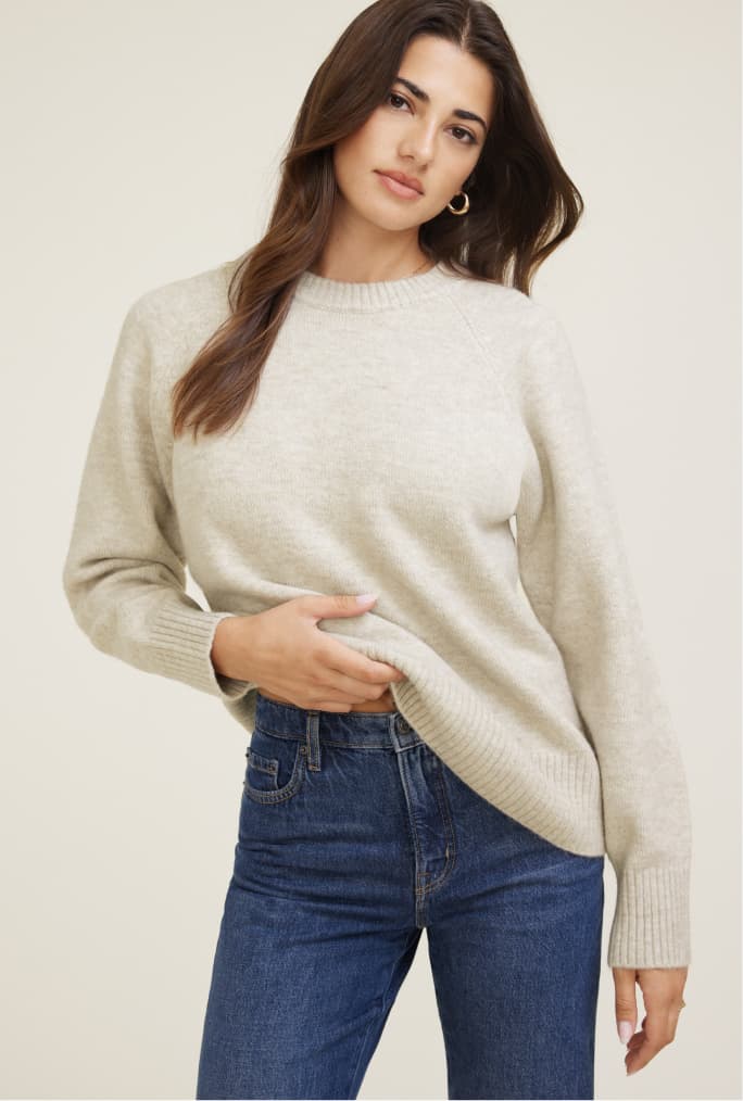 Model is wearing an off white sweater with indigo jeans.