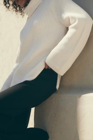 A model wears a beige knit turtleneck sweater.