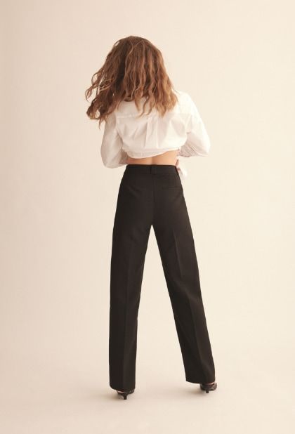 A model wears black straight leg pants with a white button down shirt.