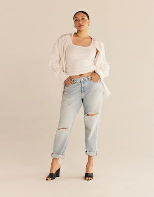 A model wears the Devyn boyfriend distressed jeans in light blue with a white tank top and a white button down shirt.
