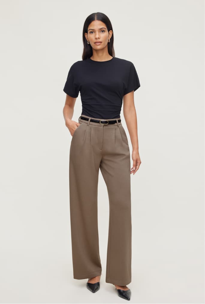 Model is wearing a black shirred T-shirt with brown dress pants.