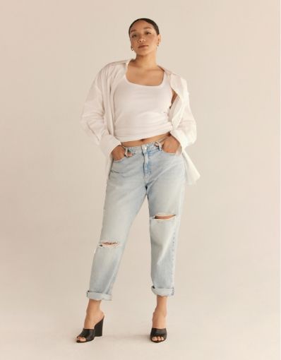 A model wears light blue distressed boyfriend jeans with a white tank top and a white button down shirt.