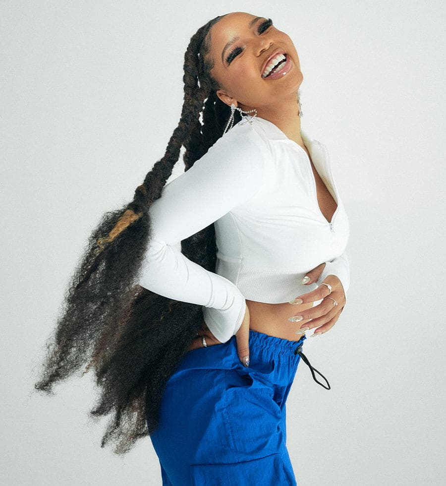 Musician Chloe Bailey wears a white zip up seamless top and blue parachute pants.