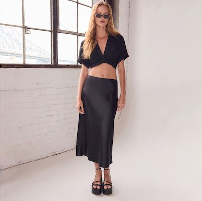 A model poses in a black cropped shirt and a black skirt.