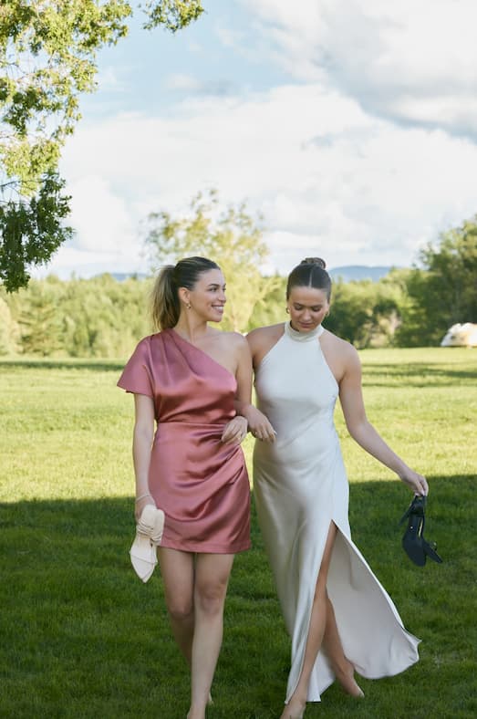 Nitsan wears the one-shoulder mini satin dress, and Sophie wears the maxi open back satin helter dress. 