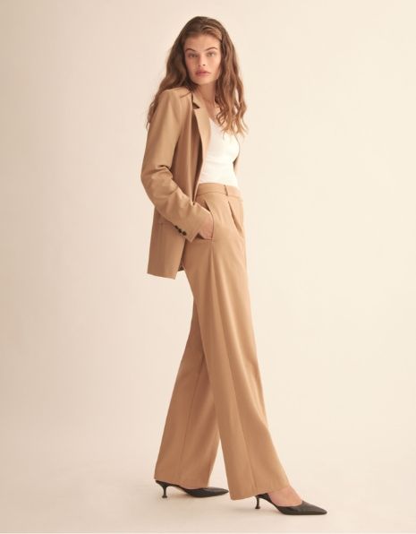 A model wears beige pleated pants and a matching blazer.