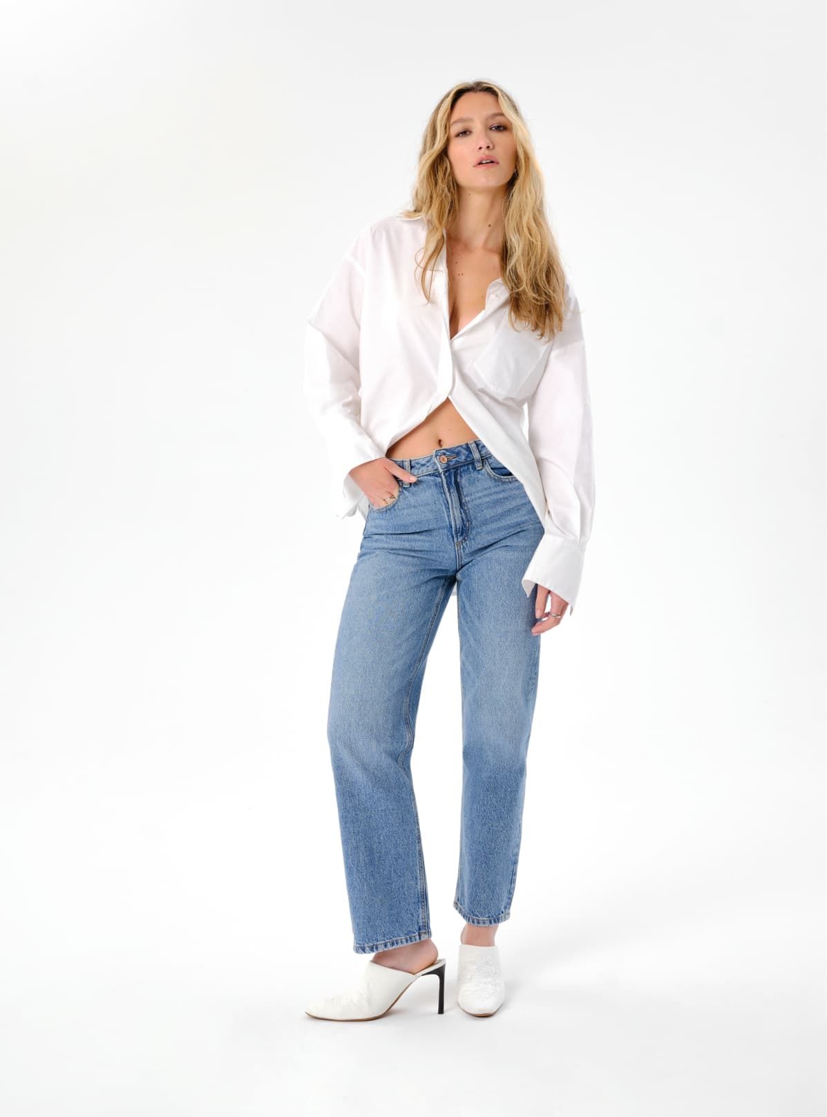 A model wears blue straight leg jeans with a white button down shirt.