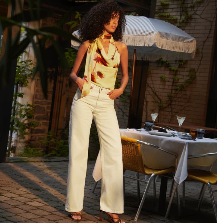 Model is wearing a yellow halter top and white jeans.