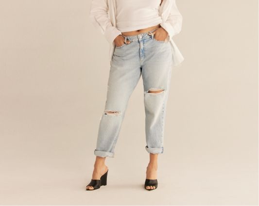 A model wears light blue distressed low-rise jeans with a white blouse