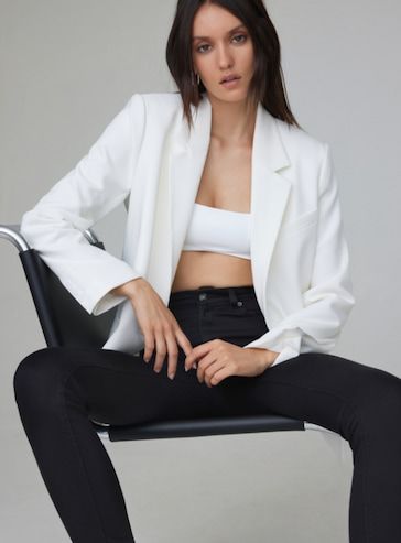 A model wears a white bra top under an open white blazer with black skinny jeans.