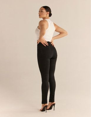 A model wears the Kate skinny jeans in ultimate black with a white tank top.