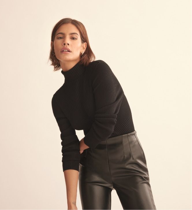 A model wears black faux leather slim pants with a black turtleneck.
