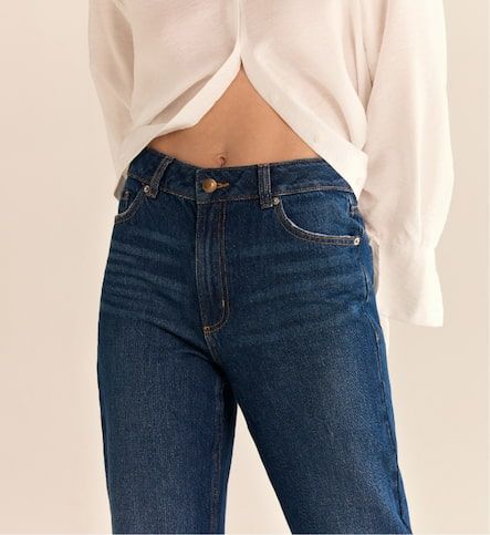 A model wears the Claudia mom jeans in dark indigo blue with a white button down shirt.