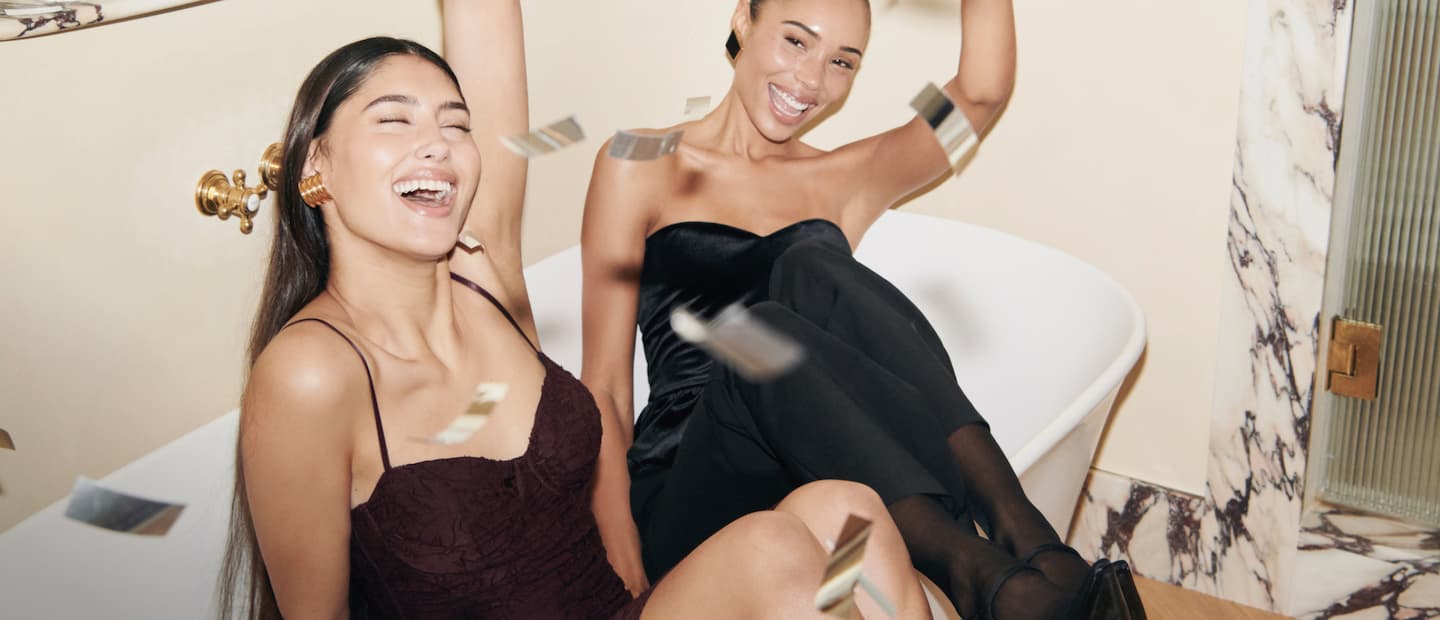 Model on the left is wearing a purple floral maxi dress. Model on the right is wearing a black velvet tube top and black pants.