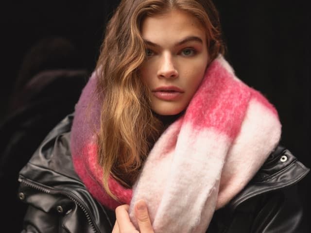A model wears a pink plaid knit scarf.