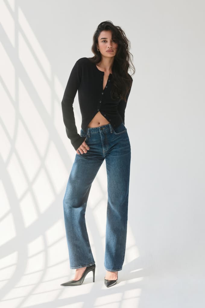 Model is wearing a black cardigan and dark blue straight leg jeans.