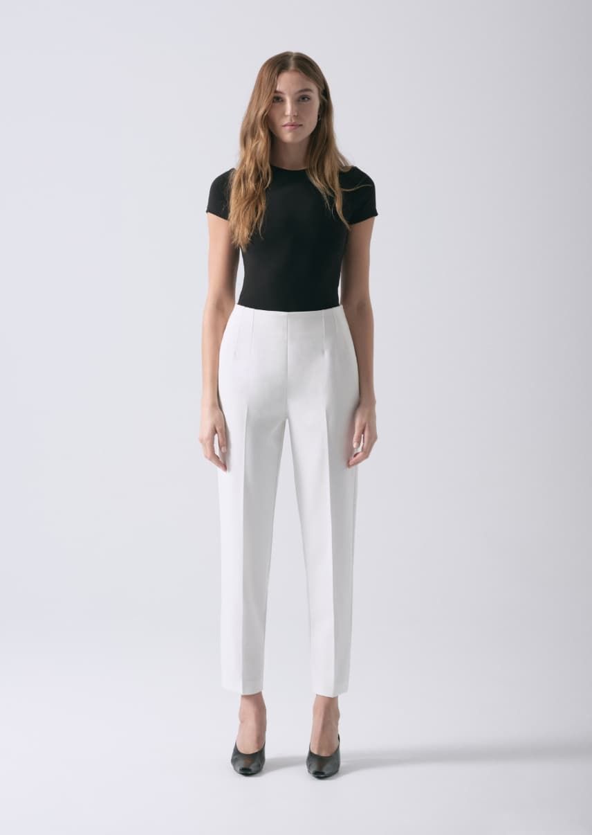A model wears white slim leg pants with a black t-shirt.