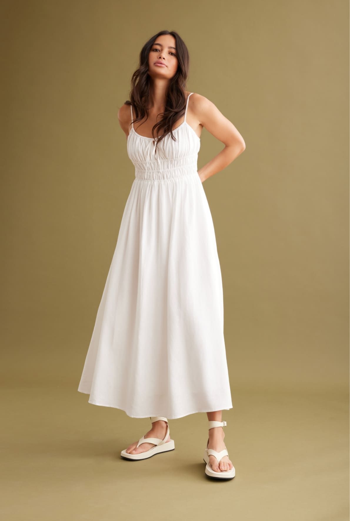 A model wears a white maxi linen dress with a ruched bust