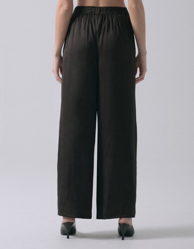 A model wears black wide leg satin pants. - back view.