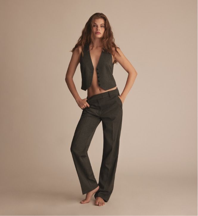 A model wears grey straight leg pants with a grey vest.