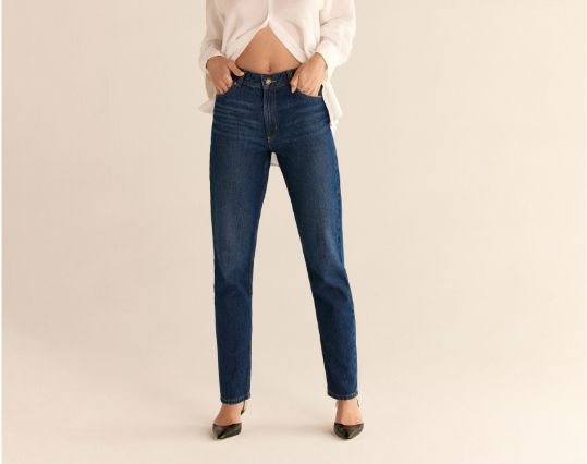 A model wears dark blue high-rise jeans with a white button down shirt