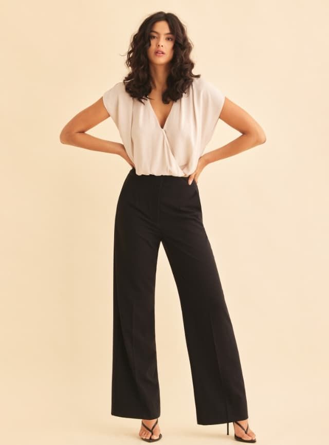 A model wears black wide leg pants with a beige short sleeve wrap blouse.