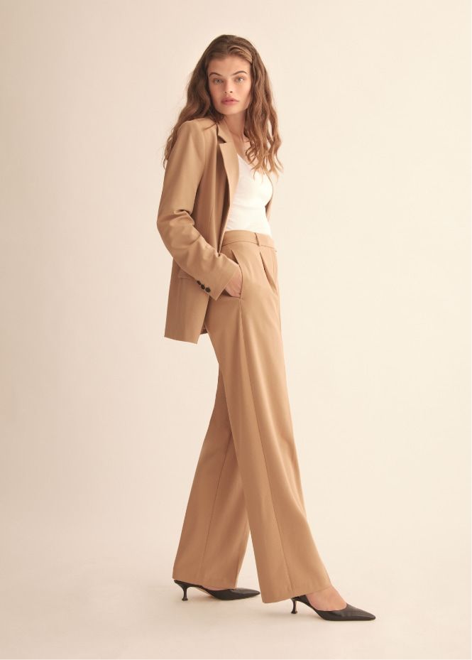 A model wears beige pleated pants and a matching blazer.