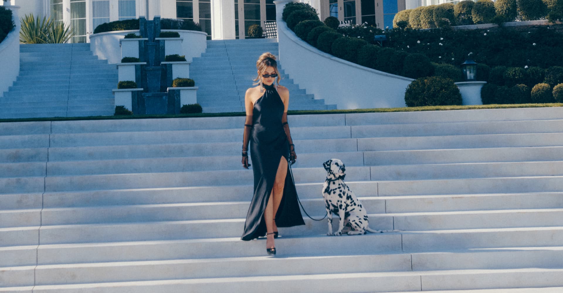 An influencer wears a black satin halter neckline dress with a leg slit.