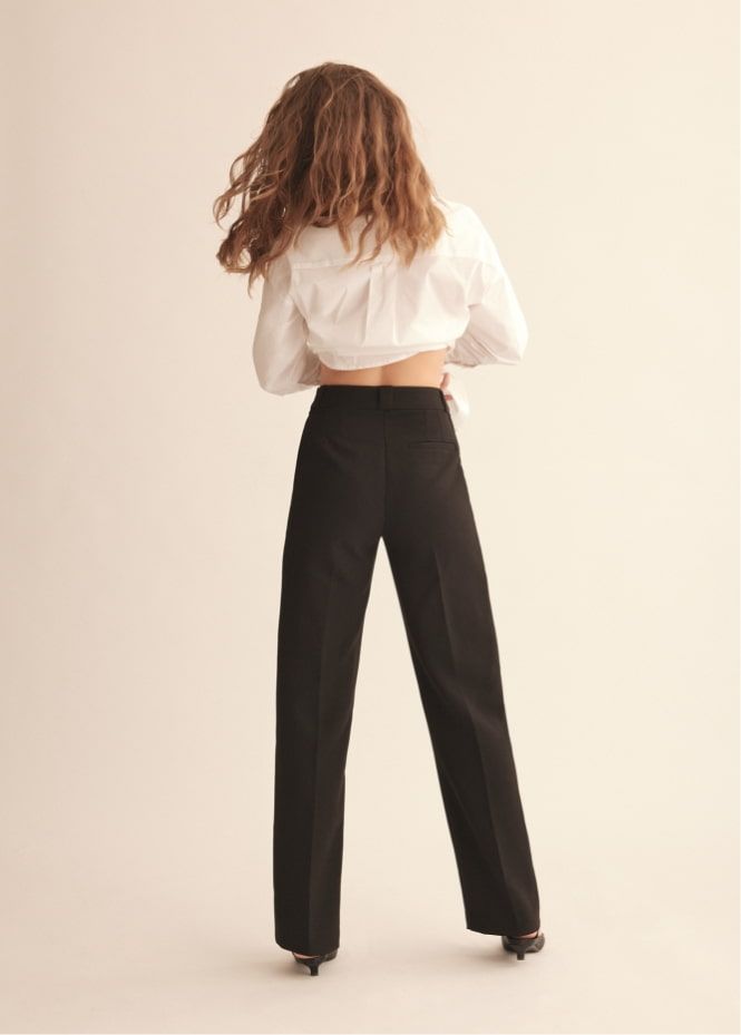 A model wears black straight leg pants with a white button down shirt.