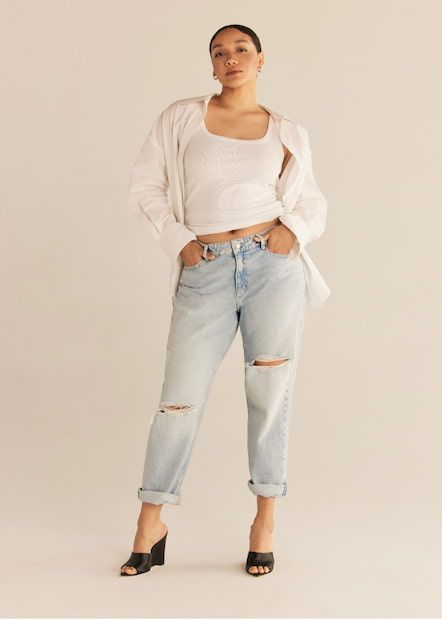 A model wears the Devyn boyfriend distressed jeans in light blue with a white tank top and a white button down shirt.